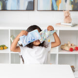 A child holds Bumkins Reusable Snack Bag, Small 2 Pack: Stitch Star-ring Up Trouble in front of their face at a white table.
