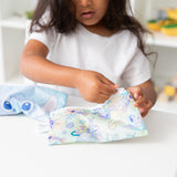 A child in white shirt unzips a Bumkins Reusable Snack Bag, Small 2 Pack: Stitch Star-ring Up Trouble at a white table.