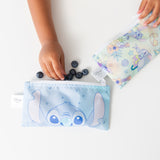 A child's hand reaches for blueberries next to Bumkins Reusable Snack Bag, Small 2 Pack: Stitch Star-ring Up Trouble on a white table.