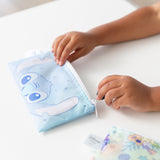 A child opens a Bumkins Reusable Snack Bag, Small 2 Pack: Stitch Star-ring Up Trouble on a white table.