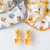 Close-up of 3 colorful printed bibs above Bumkins Silicone Chewtensils®: Winnie The Pooh on a white background.