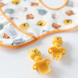 Close-up of Bumkins Silicone Chewtensils®: Winnie The Pooh on a white background, with a colorful printed bib blurred behind.