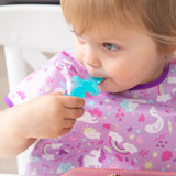 Close-up of a child in a purple unicorn bib chewing a Bumkins Silicone Chewtensils®: Blue Jelly.