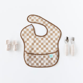 Bumkins Silicone Chewtensils®: Sand sit to the left of a tan checkered bib on a white background., with another set of utensils to the right.