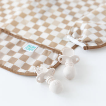 Close-up of Bumkins Silicone Chewtensils®: Sand on a white background next to a tan checkered bib.