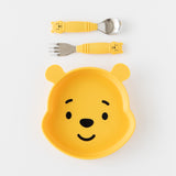 A plate and matching toddler utensils from Bumkins On-The-Go Mealtime 7-Piece Set: Pooh Bear + Friends rest on a white background.