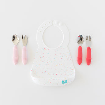 Bumkins Silicone Bib: Vanilla Sprinkle with pink handle utensils on the left and red handle utensils on the right on a white background.