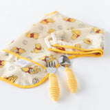 Bumkins Spoon + Fork: Pineapple lays near a folded yellow sleeved bib on a white background.