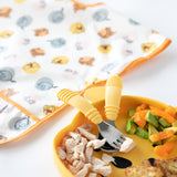 Bumkins Spoon + Fork: Pineapple on a yellow plate with chicken, avocado & veggies; patterned bib in the background adds charm.