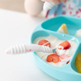 Close-up of Bumkins Spoon + Fork: Vanilla Sprinkle in a blue sectioned plate filled with yogurt and fruit on a white table.