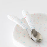 Close-up of Bumkins Spoon + Fork: Vanilla Sprinkle resting on a matching plate on a white background.