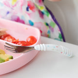 Close-up of a Bumkins Spoon + Fork: Vanilla Sprinkle resting on a pink sectioned plate with tomatoes and avocado on a white table.