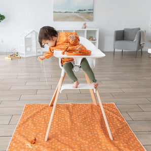A child in a high chair drops spaghetti on a Bumkins Splat Mat: Grounded underneath in a bright room.