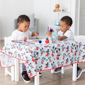 Two toddlers paint at a table covered with a splat mat from Bumkins Disney Little Ones Gift Bundle: Mickey Mouse Classic.