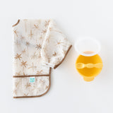 Bumkins Sleeved Bib: Palm Daze sits folded beside a yellow bowl and spoon on a white backdrop.