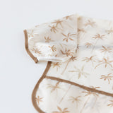 Close-up of Bumkins Sleeved Bib: Palm Daze on a white background, with focus on the white elastic cuff on the sleeve.