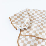 Close-up of Bumkins Sleeved Bib: Sand Check on a white background, with focus on the white elastic cuff on the sleeve.