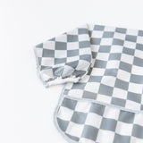 Close-up of Bumkins Sleeved Bib: Charcoal Check on a white background, with focus on the white elastic cuff on the sleeve.