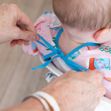 Adult hands tie the ribbon closure on Bumkins Sleeved Bib: Boots, worn by a baby in a high chair.