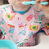 A baby enjoys feeding time while wearing Bumkins Sleeved Bib: Boots, while a drop of yogurt falls down the front of the bib.