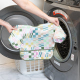 A person holds Bumkins Sleeved Bib: Motley Check in front of an open front-loading washing machine.
