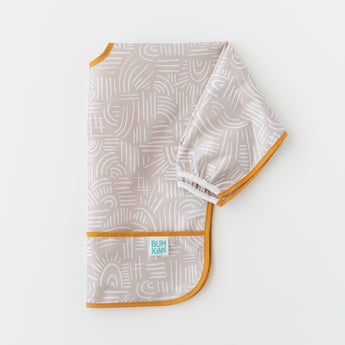 A bib from Bumkins On-The-Go Mealtime 6-Piece Set: Wander + Sand lays folded on a white background.