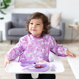 A girl wearing a purple bib in a high chair eats breakfast from Bumkins Grip Dish Essential Toddler 4-Piece Mealtime Set: Lavender.