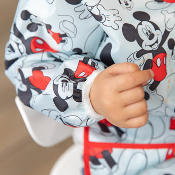 Close-up of a child wearing a Bumkins Sleeved Bib: Mickey Mouse, with focus on the elastic cuff on the sleeve.