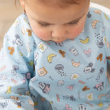A child wearing a Bumkins Sleeved Bib: Mickey + Minnie Sunny Side Up looks down with a serious expression.