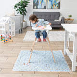 In a cozy living room with wooden floors, a child in a Bumkins Sleeved Bib: Mickey + Minnie Sunny Side Up sits in a high chair.