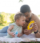 In the park, a dad and toddler explore motor skills on a blanket with Fat Brain Toy Cos Dimpl Billow Bright sensory toy.