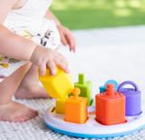A child explores sensory learning, stacking blocks with the Plugzy Shape Learning Toy by Fat Brain Toy Co, boosting fine motor skills outdoors.