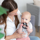 A woman holds a baby chewing a Bumkins Silicone Flat Teether: Mickey Mouse made from LFGB-grade silicone.