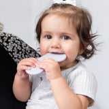 A brown-haired toddler in a light gray shirt chews on a Bumkins Silicone Teether: Nintendo SNES™ Controller for gum relief.
