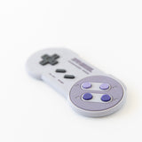 Bumkins Silicone Teether: Nintendo SNES™ Controller, featuring a gray body and purple buttons, on white background.