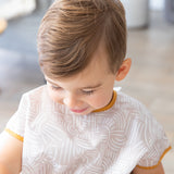 A child with light brown hair looks down while wearing a Bumkins Junior Bib: Wander.