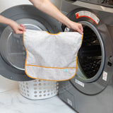A person holds a Bumkins Junior Bib: Wander in front of a front-loading washing machine.