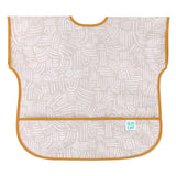 Bumkins Junior: Bib Wander features beige waterproof fabric with abstract white patterns, orange trim, and a catch-all pocket.