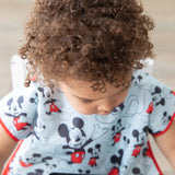 Close-up of a curly-haired child wearing a Bumkins Junior Bib: Mickey Mouse Classic looking down.