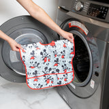 A person holds Bumkins Junior Bib: Mickey Mouse Classic in front of an open front-loading washing machine.