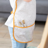 Close-up of a child in a Bumkins Short-Sleeved Smock: Wander with paint brushes in the pocket.