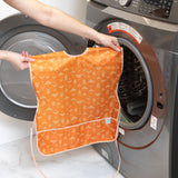 A person holds a Bumkins Short-Sleeved Smock: Grounded in front of an open front-loading washing machine.