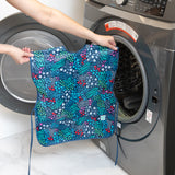 A person holds a Bumkins Short-Sleeved Smock: Animal Prints in front of an open washing machine.