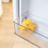 A cute Bumkins Silicone Un-Droppable Mitt Teether: Winnie the Pooh sits in the side compartment of an open refrigerator door.