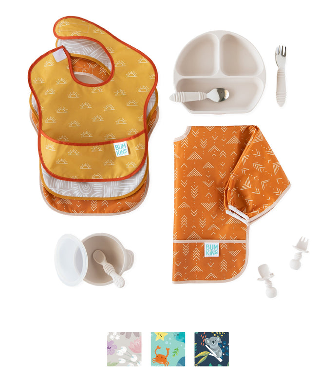 Baby feeding set with yellow and orange bibs, sectional plate, utensils, and a cup, all laid out on a white background.
