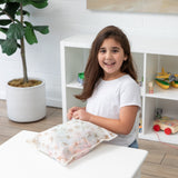 Smiling girl with her packing essentials and Bumkins Wet Bag + Wet/Dry Bag Set: Palm Daze in a bright, toy-filled room.