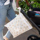 A parent in jeans pushes a stroller with a Bumkins Wet Bag: Palm Daze attached to the handle.