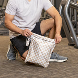 A man kneels on a gym floor, unzipping a bag from Bumkins Wet Bag + Wet/Dry Bag Set: Sand Check.