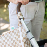 Close-up of a person in white pants pushing a stroller with a Bumkins Wet Bag 2 Pack: Palm Check attached to the handle.