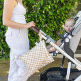 A woman pushes a stroller with a baby; a Bumkins Wet Bag + Clear Travel Bag 3 Pack Set (Sand Check) hangs from the handle.